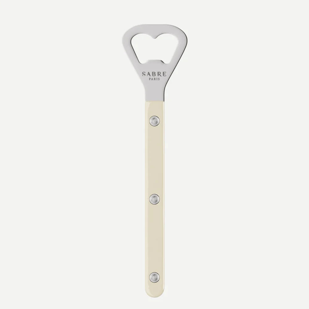 A vertical bottle opener with a cream-colored handle and a silver metal head featuring a heart-shaped cutout. The brand name 'SABRE PARIS' is printed on the metal head.