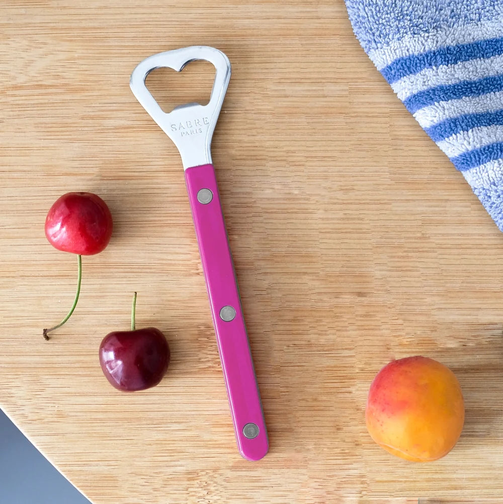 Pink bottle opener with a hole on a wooden surface with cherries and an apricot.