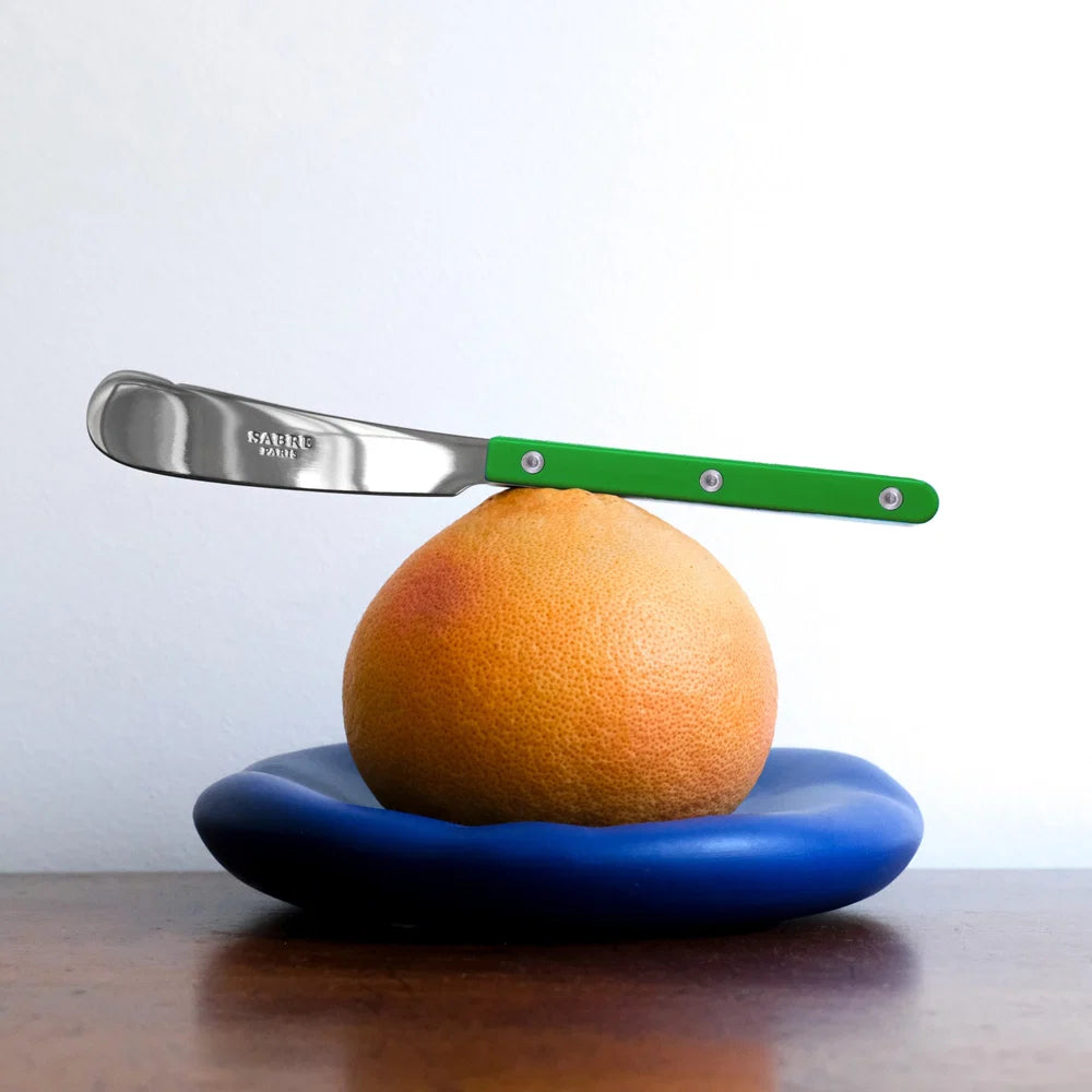 Knife balancing on an orange with a blue plate underneath, on a white background