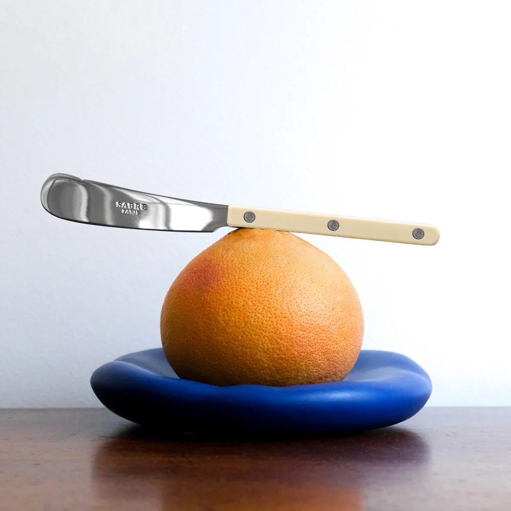 Knife balancing on an orange on a blue plate with a white background