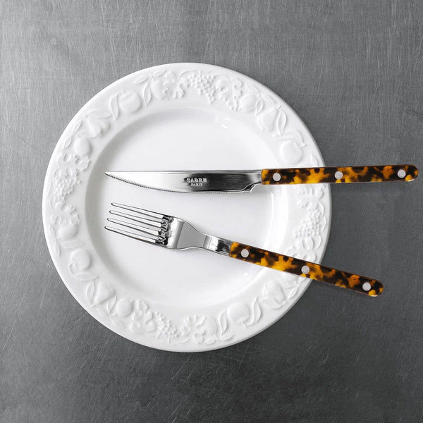 White plate with silver knife and fork with tortoiseshell handles on a gray surface