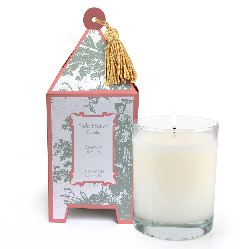 Candle in glass container next to pagoda box with green and pink pattern on white background 