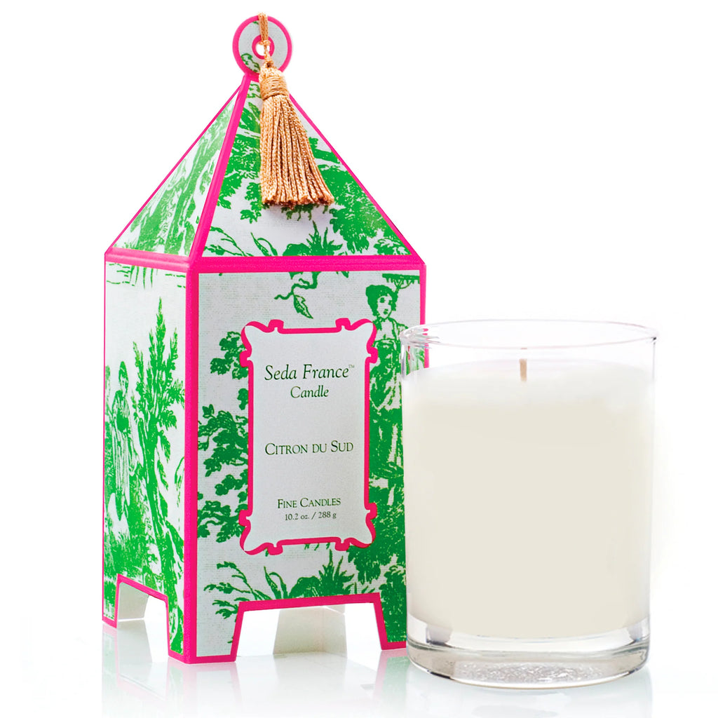 Candle in glass container next to pink and green patterned pagoda box on white background