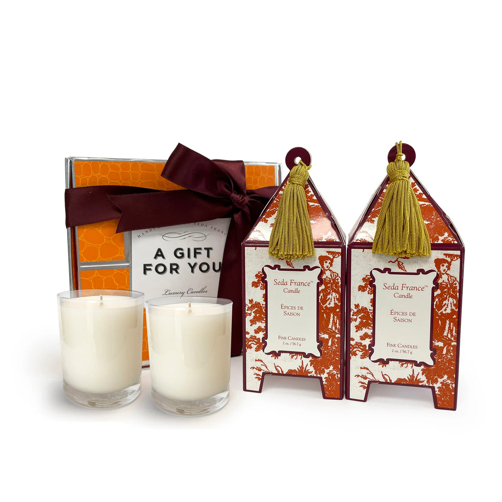A luxury candle gift set from Solis France Candles, featuring two white soy candles in clear glass holders, two matching orange and white patterned decorative boxes with gold tassels, and an orange gift box tied with a dark burgundy ribbon that reads 'A GIFT FOR YOU'.
