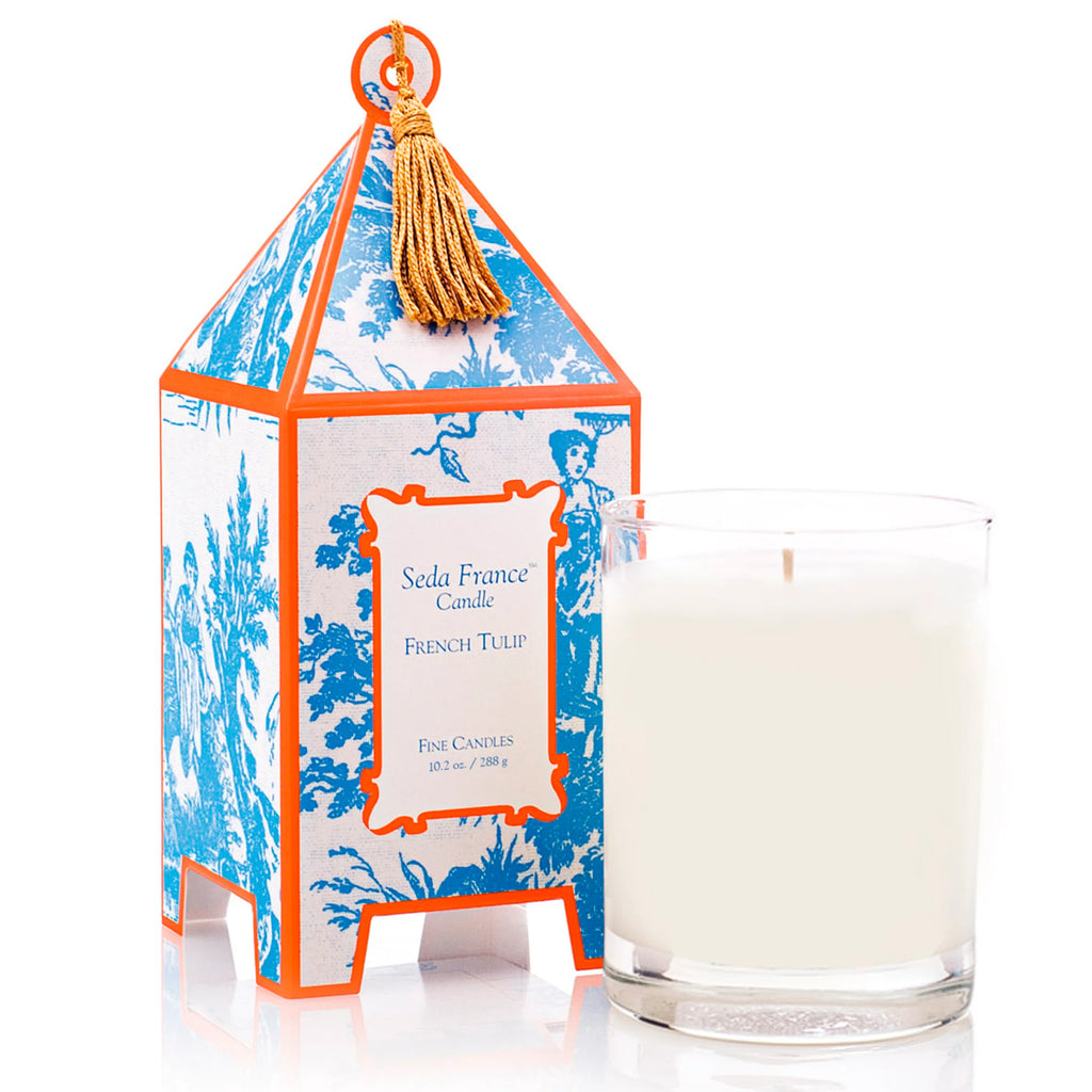 Candle in glass container next to orange and blue patterned pagoda box on white background