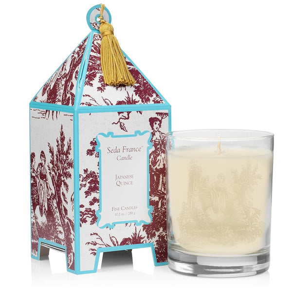 Candle in glass container next to maroon and light blue patterned pagoda box on white background