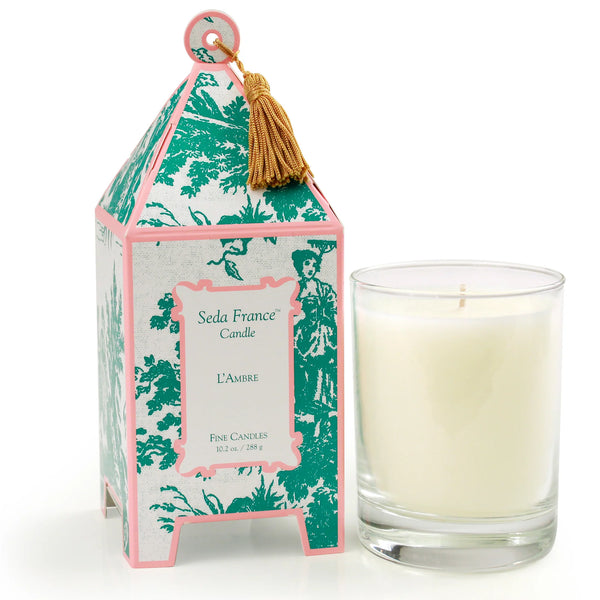 Candle in glass container next to pink and green patterned pagoda box on white background 