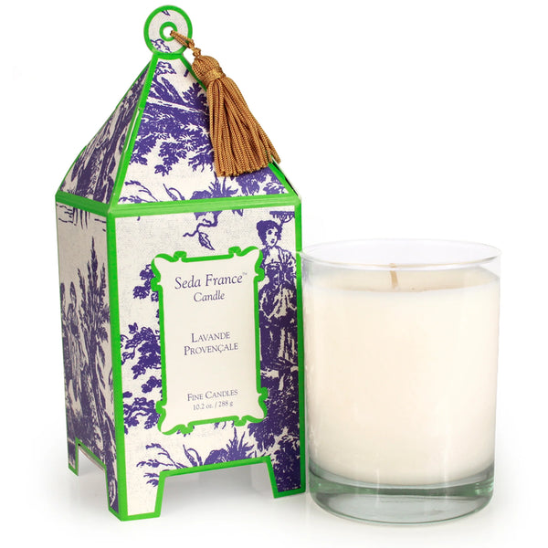 Candle in glass container next to green and purple patterned pagoda box on white background