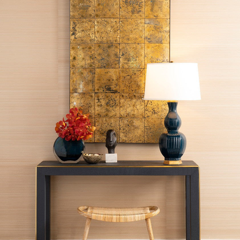 Decorative console table with a lamp, sculpture, and flowers against a beige wall with a gold-framed artwork.