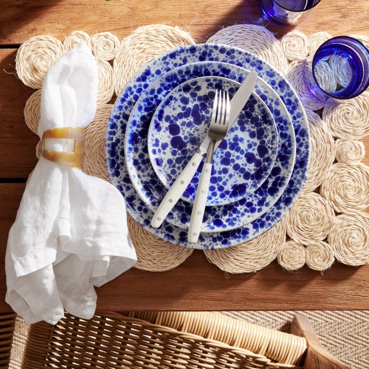 Blue and white dinner plates table setting with napkin, glassware, and silverware on rustic farmhouse table.